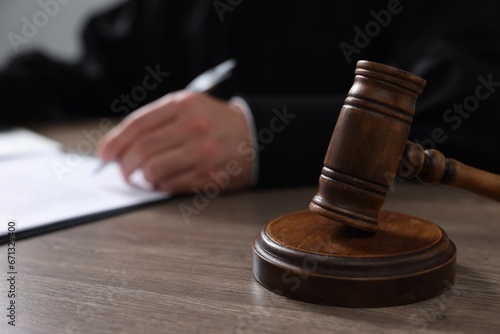 Judge with gavel writing in papers at wooden table, closeup