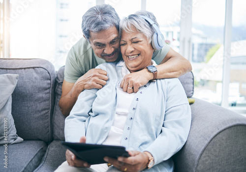 Senior, hug and couple with a tablet for a website, streaming music in home living room. Laughing, sofa and an elderly man and woman with a movie or funny video on technology or listening together