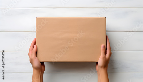 Top view of beige parcel cardboard box in a man hands with blank space on light white wooden surface. Messenger and delivery service concept. © cabado