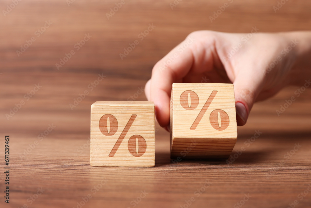 Woman arranging cubes with percent signs on wooden background, closeup Woman arranging cubes with percent signs on wooden background, closeup