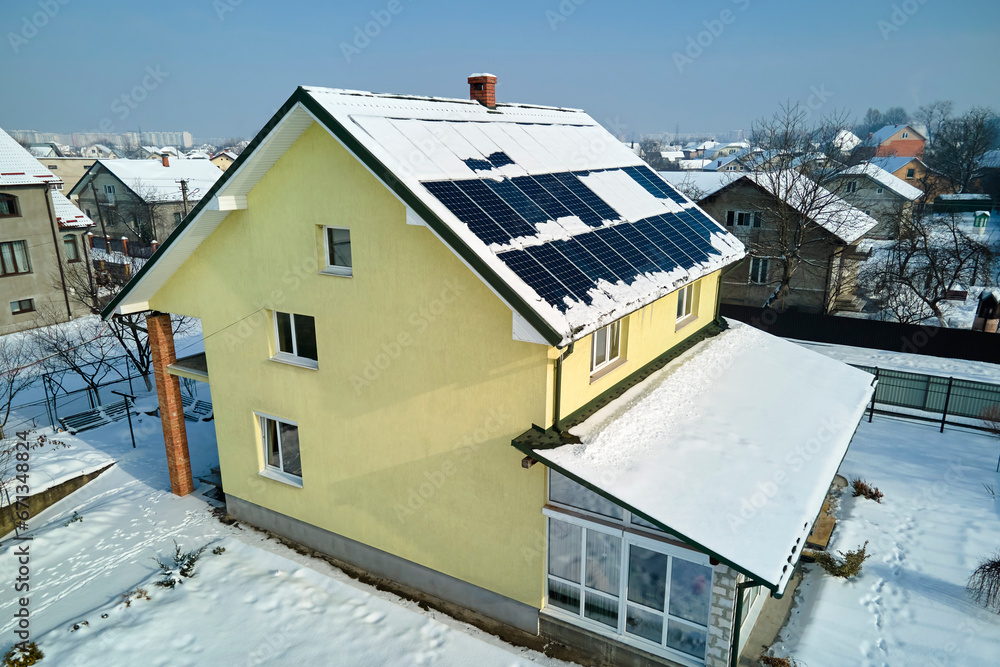 Aerial view of house roof with solar panels covered with snow melting down in winter end for producing clean energy. Concept of low effectivity of renewable electricity in northern region
