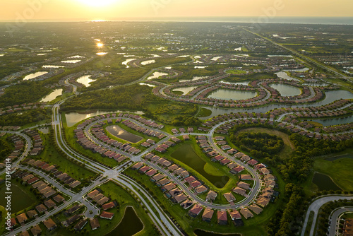 Aerial view of tightly packed homes in Florida closed living clubs with lake water in the middle. Family houses as example of real estate development in american suburbs