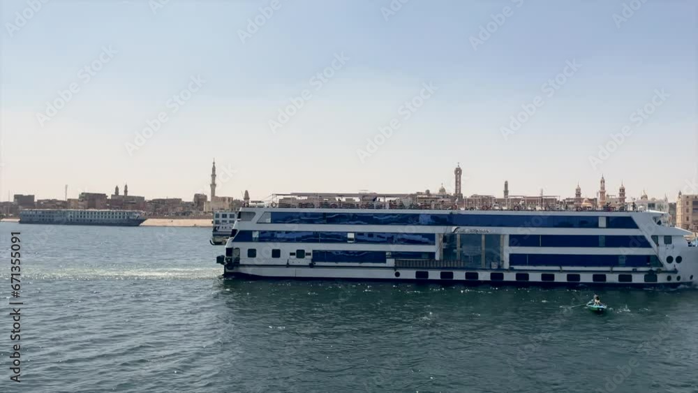 CRUISE SHIP NAVIGATES ON THE NILE RIVER WITH EGYPTIAN CITY IN THE BACKGROUND IN EGYPT CRUISE SHIP NAVIGATES ON THE NILE RIVER WITH EGYPTIAN CITY IN THE BACKGROUND IN EGYPT