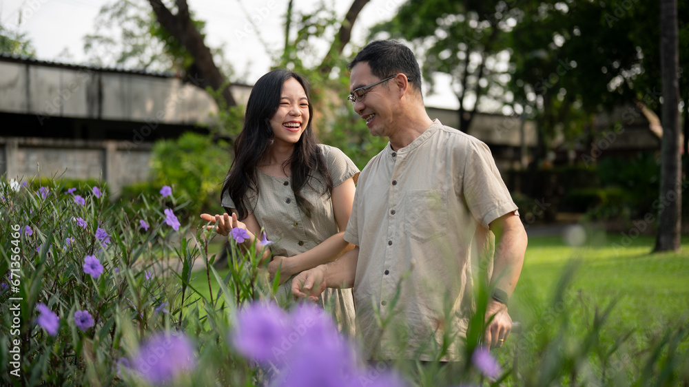 A pretty Asian daughter and her dad are enjoying talking while strolling in their courtyard garden.