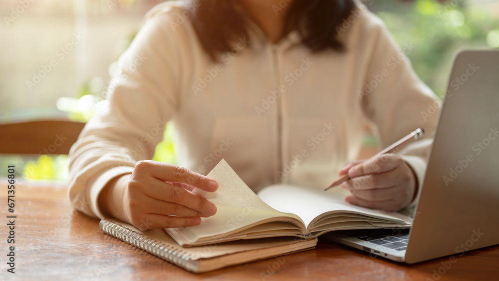 An Asian female student holding a pencil and writing in a book while studying an online class. An Asian female student holding a pencil and writing in a book while studying an online class.