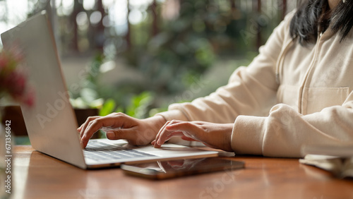 Close-up side view image of a woman working on her laptop at a table indoors, typing on the keyboard