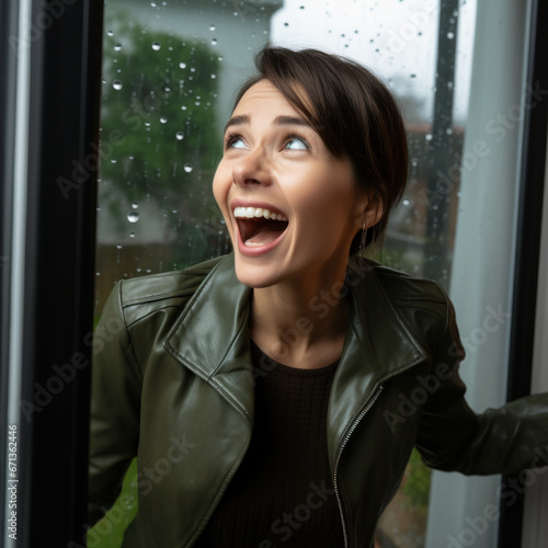 woman in green leather coat is excited with big smile in front of the window with rain on it