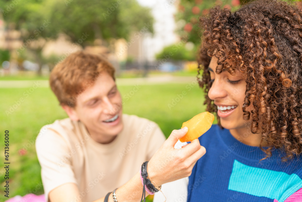 Man feeding his partner during picnic in a park Man feeding his partner during picnic in a park