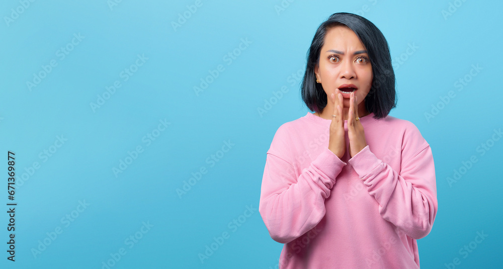 Shocked Asian woman covering mouth with palm isolated on blue ba Shocked Asian woman covering mouth with palm isolated on blue ba