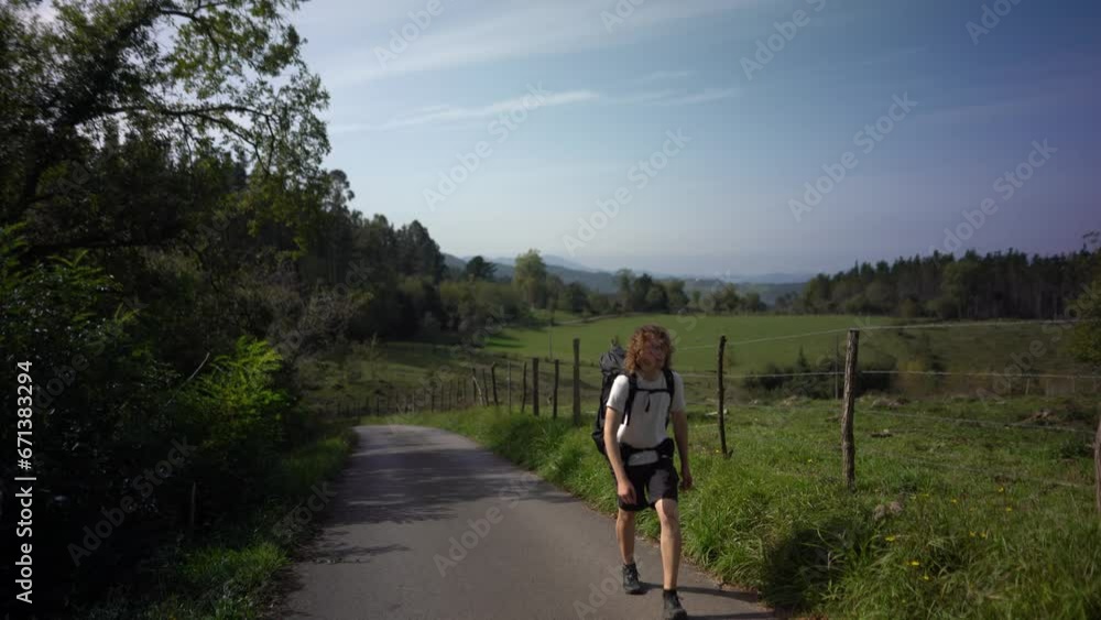Hiking man tightens backpack strap walking by field forest countryside Hiking man tightens backpack strap walking by field forest countryside