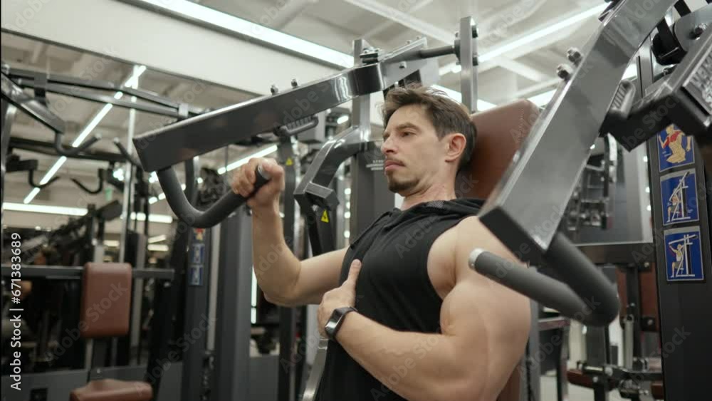 Muscular Man in 40s Doing One Hand Seated Chest Press in Health Club Muscular Man in 40s Doing One Hand Seated Chest Press in Health Club