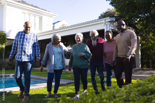 Happy diverse group of senior friends walking next to pool in sunny garden