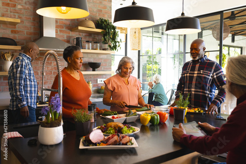 Happy diverse group of senior friends preparing meal in sunny kitchen at home