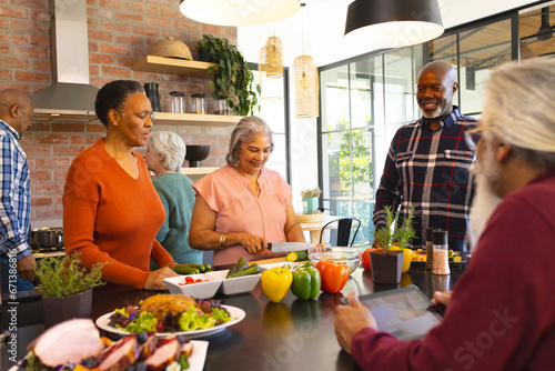 Happy diverse group of senior friends preparing meal in sunny kitchen at home
