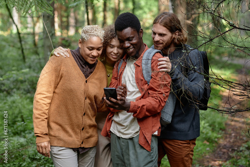 Group of friends examining online map on smartphone during their hiking in the forest