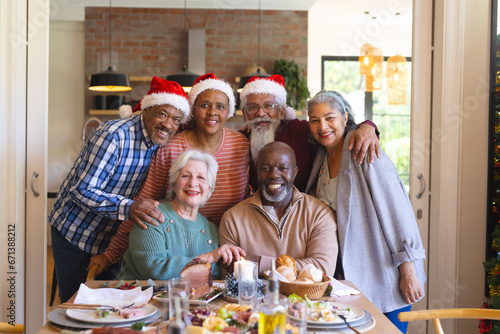 Happy diverse group of senior friends posing to picture at christmas dinner in sunny dining room