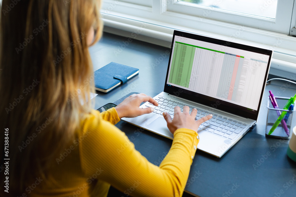 Focused caucasian woman sitting at desk, working from home and using laptop in sunny room Focused caucasian woman sitting at desk, working from home and using laptop in sunny room
