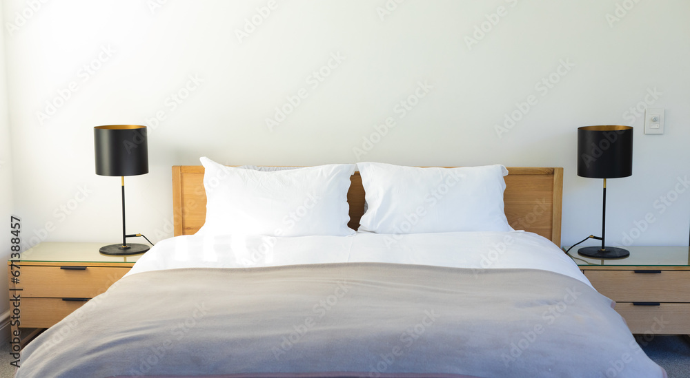 Bed with gray bedspread, white pillows and black lamps on nightstands in sunny bedroom