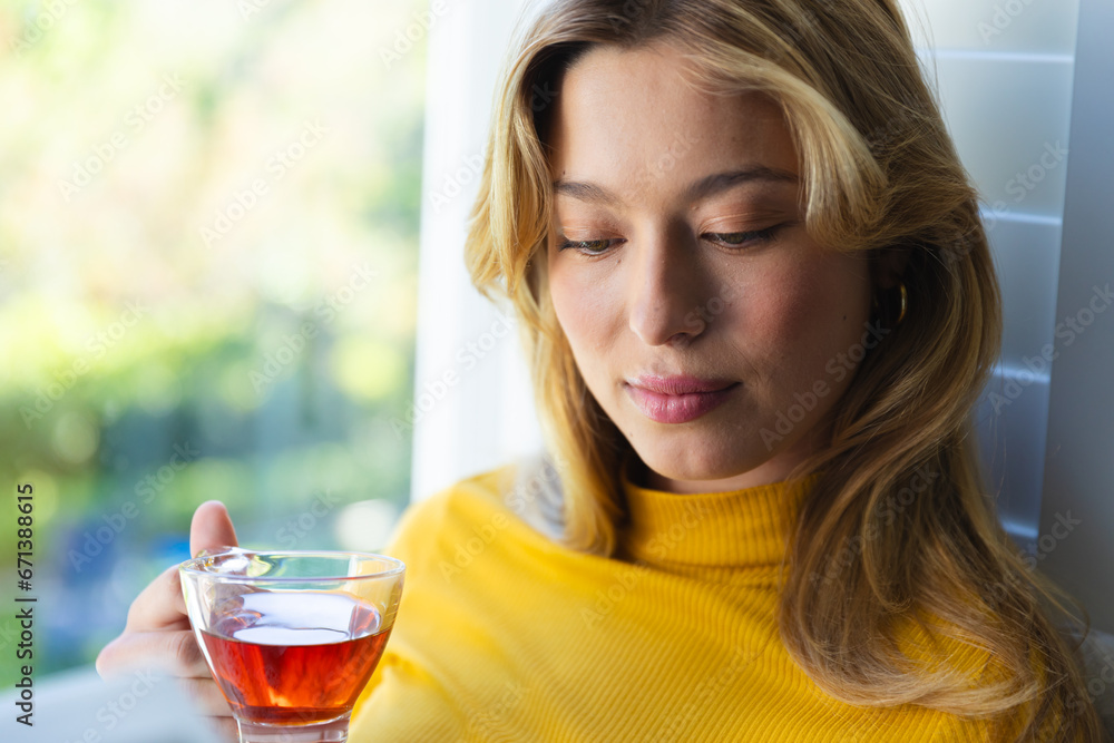 Happy caucasian woman sitting on couch with tea and looking down in sunny room at home Happy caucasian woman sitting on couch with tea and looking down in sunny room at home