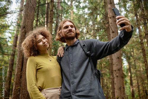 Young couple making selfie portrait on smartphone while walking in the forest © AnnaStills