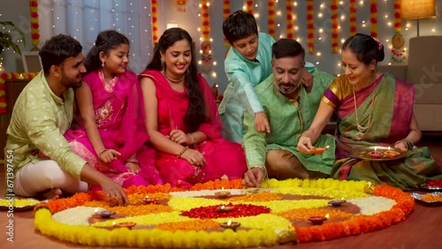 Group of Indian family members decorating Flower rangoli using Diya lamps at home for diwali celebration - concept of holiday gathering, traditional custom and rituals.