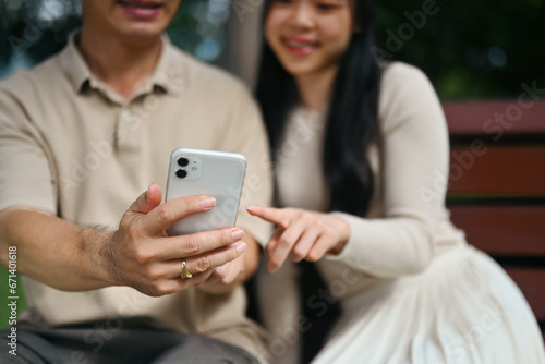 Smiling young woman and middle age father watching video on mobile phone while sitting on a park bench