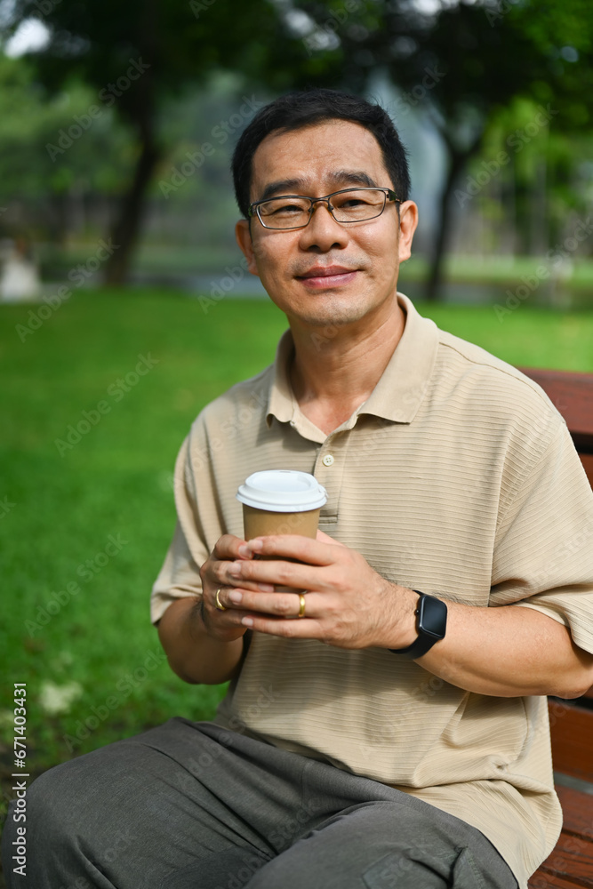 Portrait of pleased middle aged man sitting on park bench and drinking coffee Portrait of pleased middle aged man sitting on park bench and drinking coffee