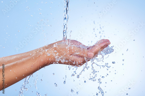 Hands, water splash and wash for skincare hygiene or hydration against a blue studio background. Closeup of hand with liquid drops, shower or washing for clean wellness or natural sustainability