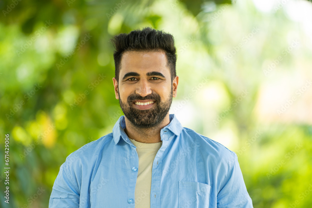 portrait shot of Happy smiling indian man standing by looking at camera at park - concept of successful, confident and positive emotion portrait shot of Happy smiling indian man standing by looking at camera at park - concept of successful, confident and positive emotion