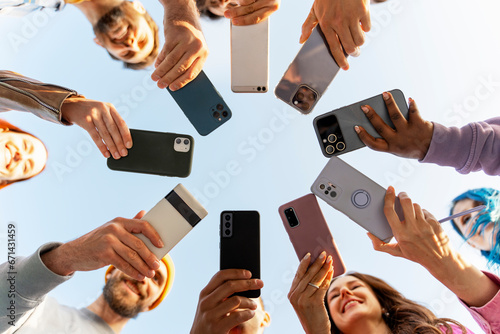 Canvas-taulu Many people, modern smiling friends holding mobile phones using mobile app standing in circle on the street, selective focus