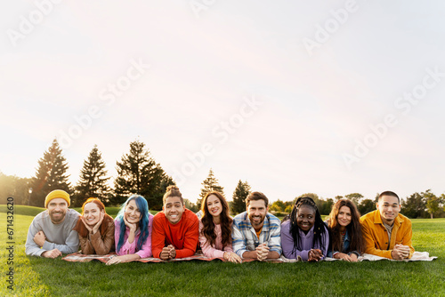 Group portrait smiling multiethnic friends lying on grass in green park. Happy attractive stylish men and women looking at camera spending time together on nature, copy space.Diversity, friendship 
