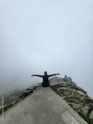 donna seduta sulla cima di una montagna tra la nebbia a braccia aperte photo