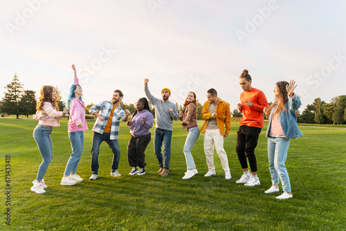 Group of happy international friends wearing colorful clothing dancing on corporate party in green park  having fun. Diversity  friendship  positive lifestyle concept