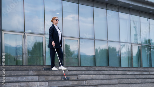 Blind business woman descending stairs with a tactile cane from a business center.