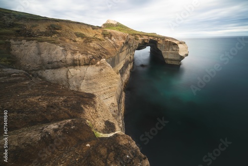 Stunning landscape featuring an imposing arch situated on a rugged cliff. Tunnel Beach, New Zealand
