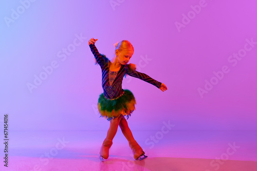 Beautiful, adorable little girl, child in stage costume dancing, performing figure skating against gradient pink purple background in neon. Concept of childhood, figure skating sport, hobby, school photo