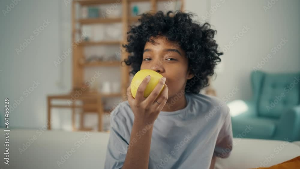Attractive cute young woman eating apple. Portrait of happy african american girl biting and eating ripe green apple, looking at camera at home interior. Concept enjoy healthy diet and lifestyle. Attractive cute young woman eating apple. Portrait of happy african american girl biting and eating ripe green apple, looking at camera at home interior. Concept enjoy healthy diet and lifestyle.