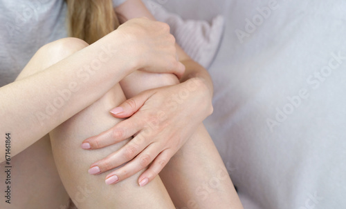 Young woman hugged her knees sitting on the bed. Depression, stress, pain, health problems. Close-up. Selective focus.