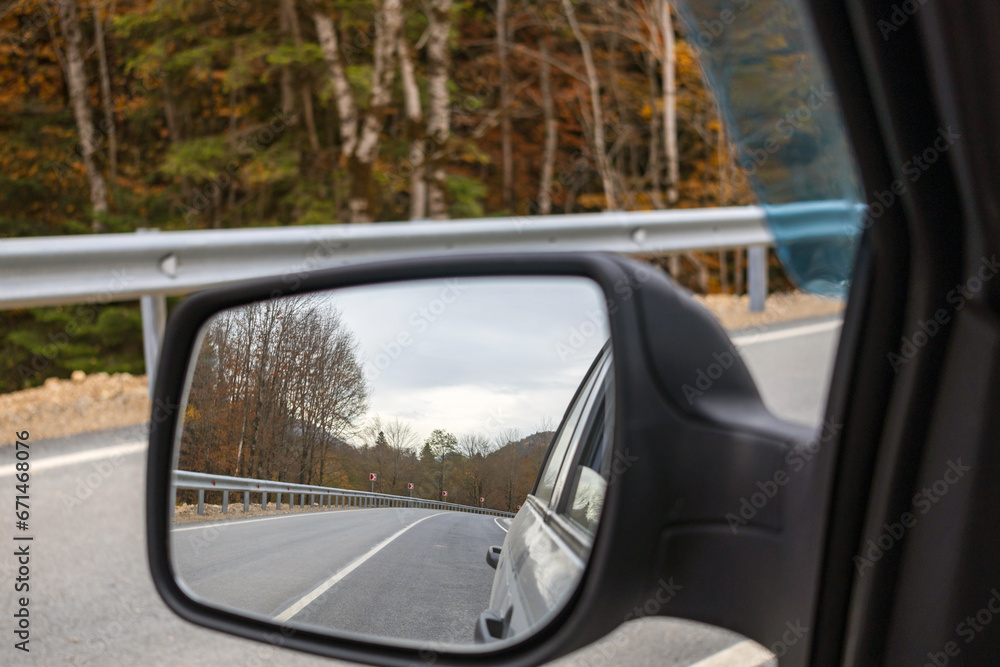Car rear view mirror. Beautiful scene of autumn trees and road in the mirror