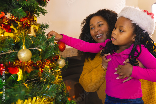 Happy african american mother and daughter decorating christmas tree at home, copy space photo