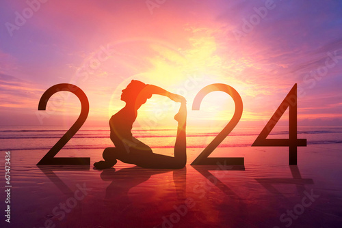 Happy new year card 2024. Silhouette of healthy girl doing Yoga One Legged Pigeon pose on tropical beach with sunset sky background, woman practicing yoga as a part of the Number 2024 sign.