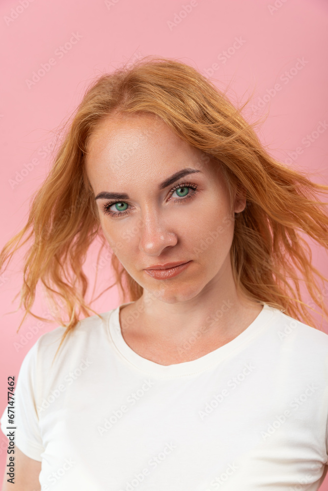 Confident look of a beautiful green-eyed woman with red hair. Attractive young woman on pink background. Close-up, vertical frame Confident look of a beautiful green-eyed woman with red hair. Attractive young woman on pink background. Close-up, vertical frame