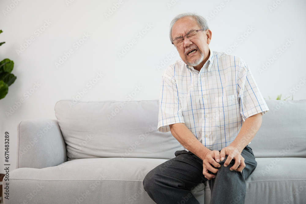 senior man suffering from knee ache on sofa