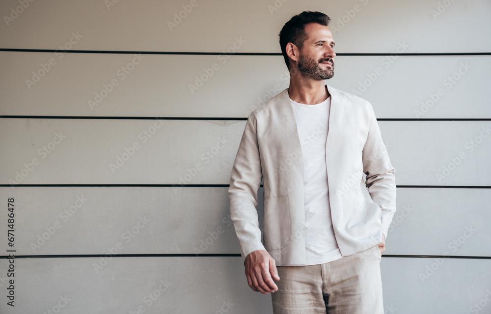 Portrait of handsome confident stylish hipster lambersexual model. Sexy modern man dressed in elegant suit. Fashion male posing in the street near urban wall. In sunglasses