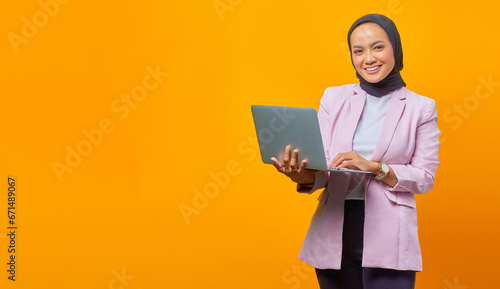 Portrait of smiling asian woman holding laptop and looking at ca