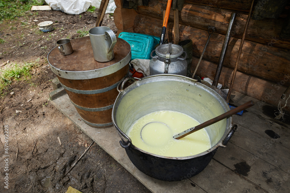 Fototapeta premium A mountain shepherd cooks cheese in a cauldron over a fire. Traditional cheese making in the mountains.