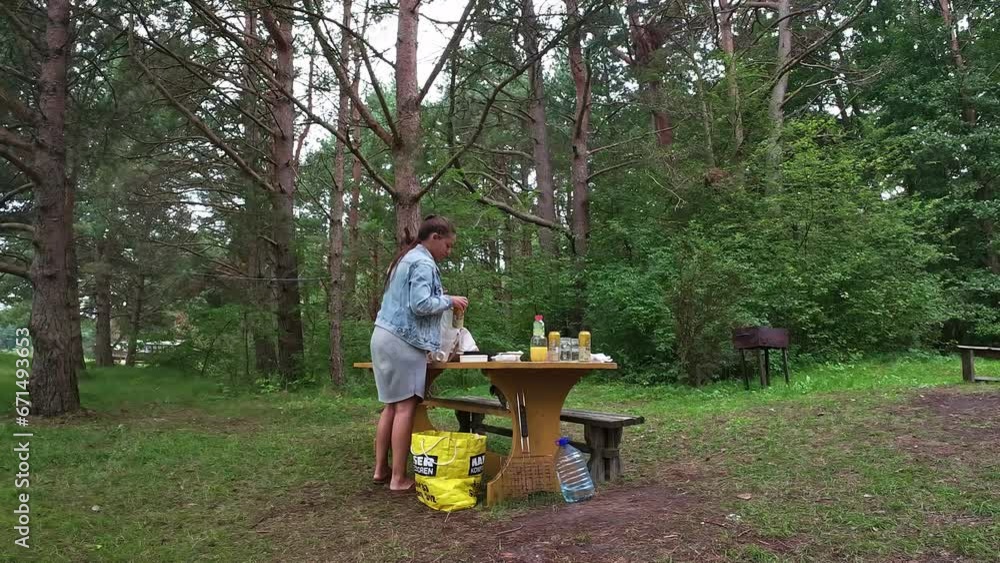 Shot of young lady collecting tin can front an outdoor picnic table and putting it into a white trash bag for recycling.