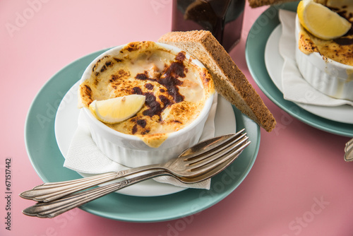 Typisches DDR Würzfleisch Ragout Fin mit Käse überbacken, Zitrone, Toast Brot und Worcester Sauce  in Auflaufform Schale auf grün Teller und pink rosa Hintergrund