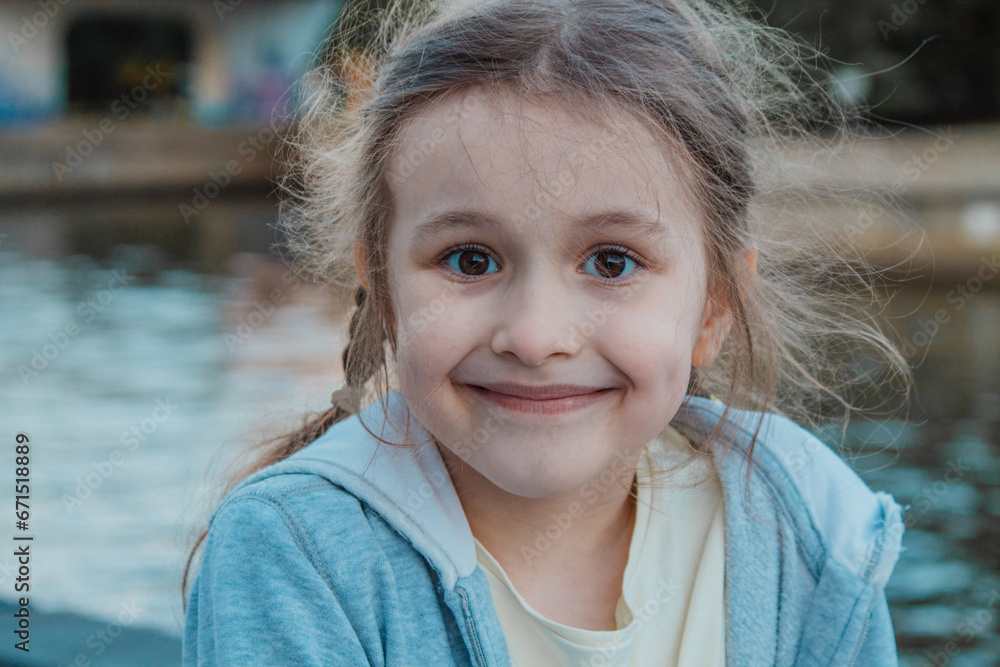 A little girl with kind brown eyes, smiling and looking at you. There is a pond in the background. The concept of a carefree happy childhood under a peaceful sky. A little girl with kind brown eyes, smiling and looking at you. There is a pond in the background. The concept of a carefree happy childhood under a peaceful sky.