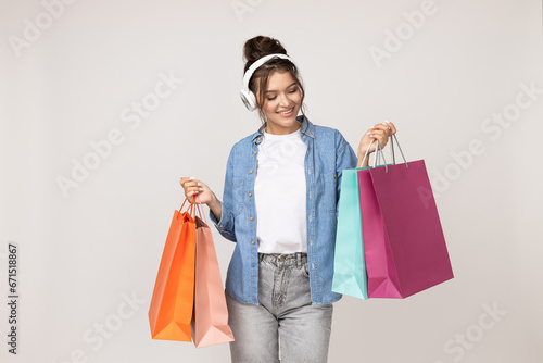 Happy young woman in headphones and with colored paper bags on white background